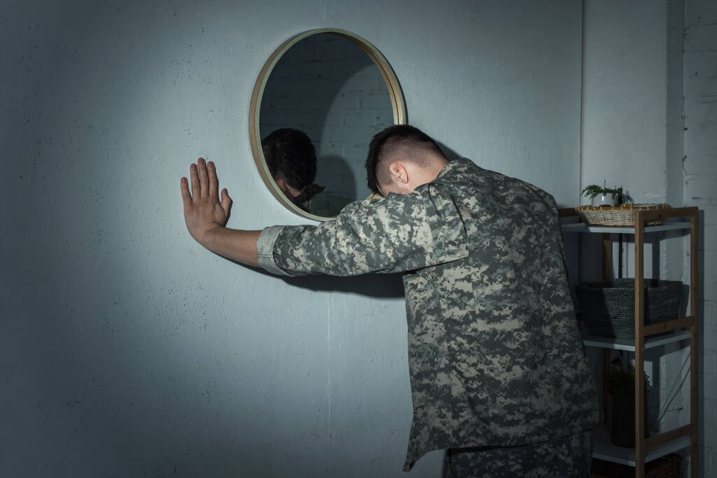 Στρατιωτικός βετεράνος με ψυχική ασθένεια στέκεται κοντά στον καθρέφτη στο σπίτι τη νύχτα  - Φωτογραφία, εικόνα