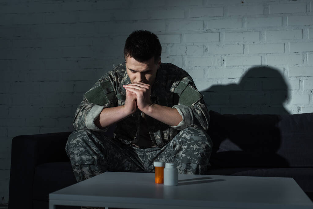 Militärangehöriger mit geistiger Distanzierung sitzt nachts in der Nähe von Tabletten  - Foto, Bild