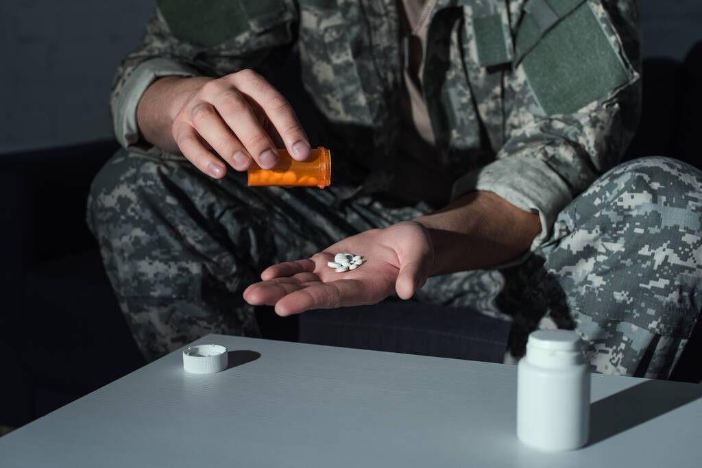 Vista recortada de soldado con trastorno de estrés postraumático sosteniendo pastillas en casa  - Foto, imagen