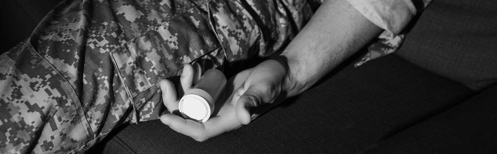 monochromatyczne zdjęcie wojskowego w kamuflażu trzymającego antydepresanty w domu, baner  - Zdjęcie, obraz