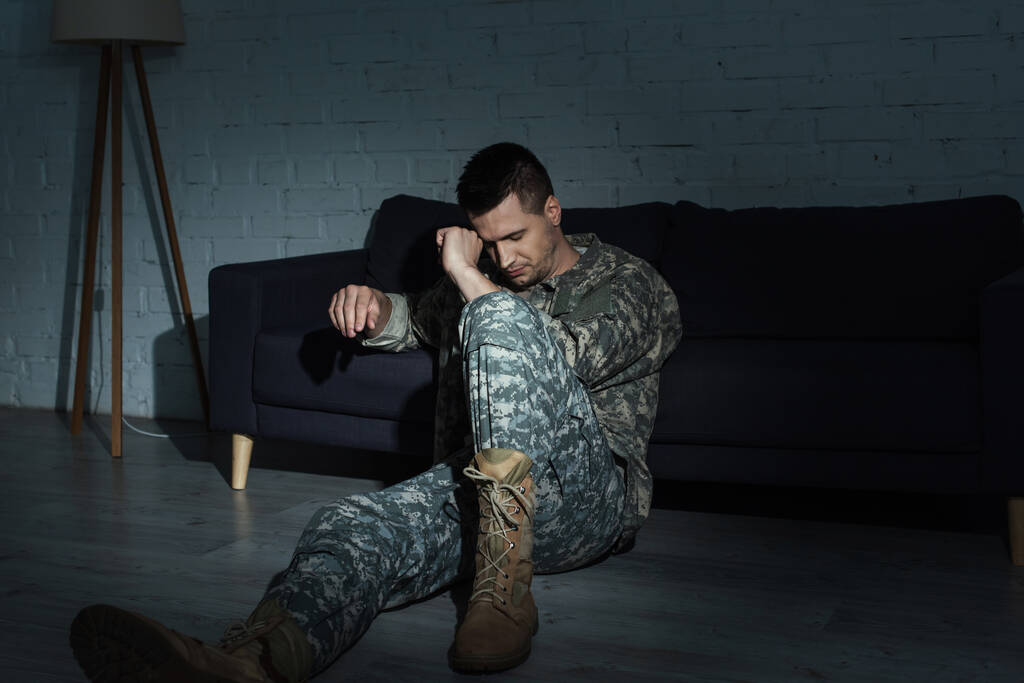 καταθλιπτικός στρατιώτης με στρατιωτική στολή που κάθεται στο πάτωμα ενώ υποφέρει από μετατραυματική διαταραχή άγχους - Φωτογραφία, εικόνα