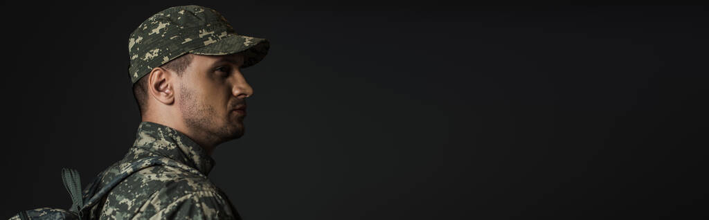 soldato patriottico in uniforme mimetica in piedi con zaino isolato su nero, stendardo  - Foto, immagini