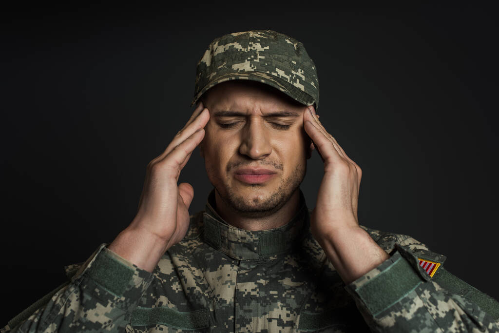 soldado patriótico em uniforme de camuflagem e boné sofrendo de tept isolado em preto  - Foto, Imagem