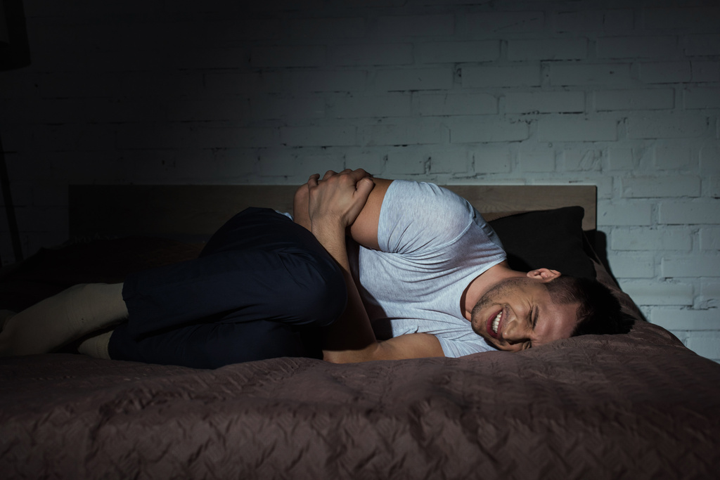 Młody człowiek z zamkniętymi oczami cierpiący na stres pourazowy leżący w nocy na łóżku  - Zdjęcie, obraz