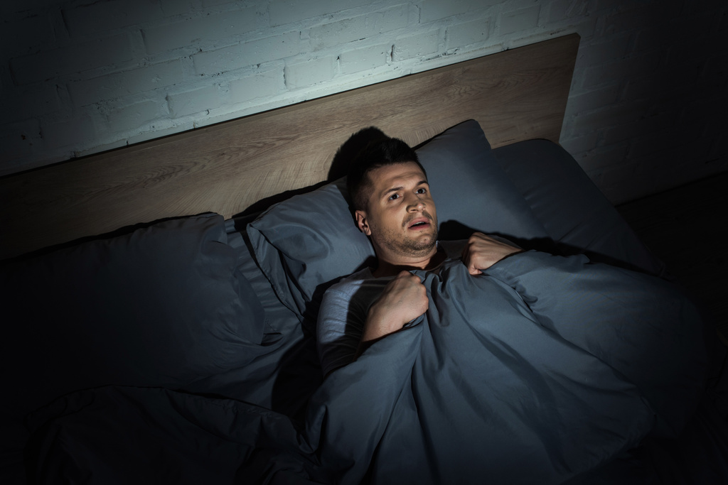 pohled na vyděšený muž trpící záchvaty paniky a nespavosti při ležení pod přikrývkou  - Fotografie, Obrázek