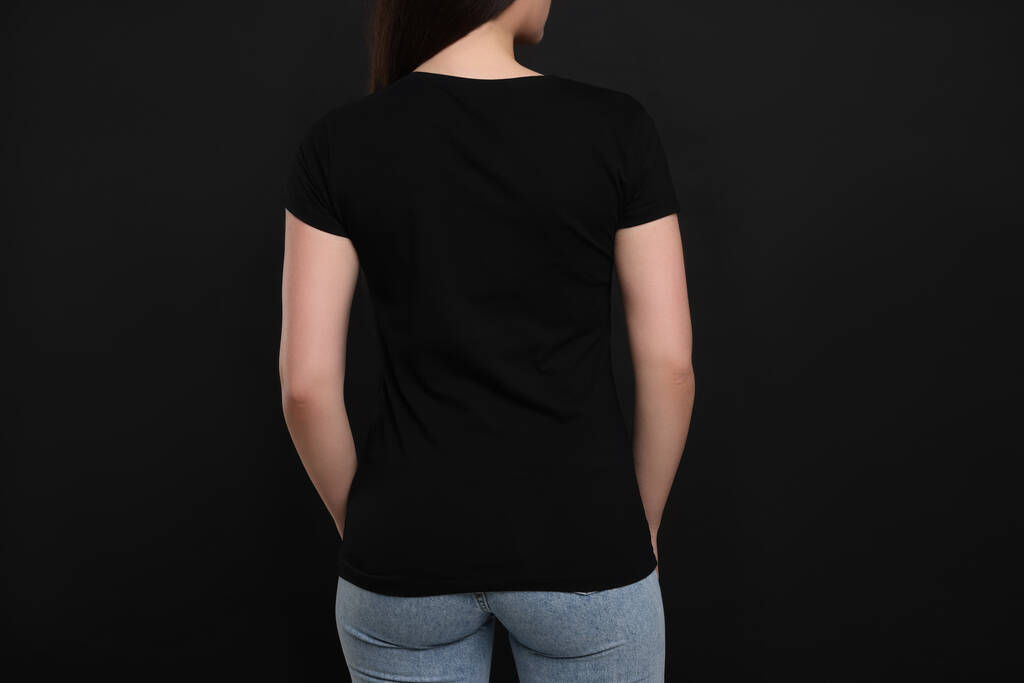 Fekete pólót viselő nő sötét háttéren, visszapillantás - Fotó, kép