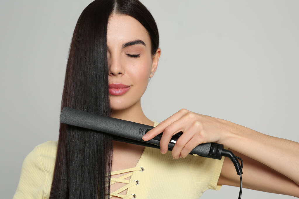 Beautiful woman using hair iron on light grey background - Photo, Image