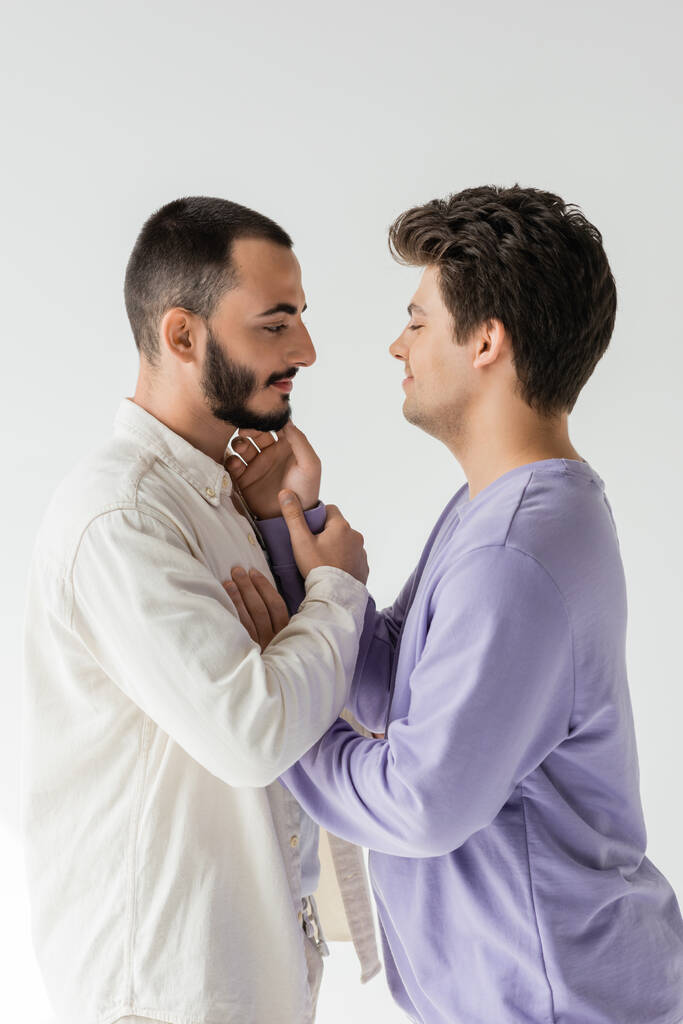 Side näkymä ikionnellinen brunette homoseksuaalinen mies suljetut silmät koskettaa poski parrakas poikaystävä rento vaatteita eristetty harmaa  - Valokuva, kuva