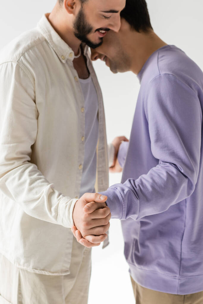 Verschwommenes und lächelndes gleichgeschlechtliches Paar in lässiger Kleidung, das sich im Gespräch an den Händen hält, während es isoliert auf grau steht  - Foto, Bild