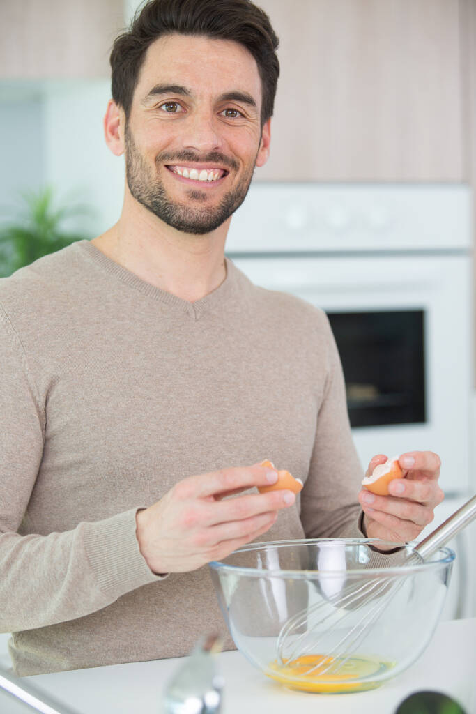 pohledný muž rozbíjí vejce do průhledné misky - Fotografie, Obrázek