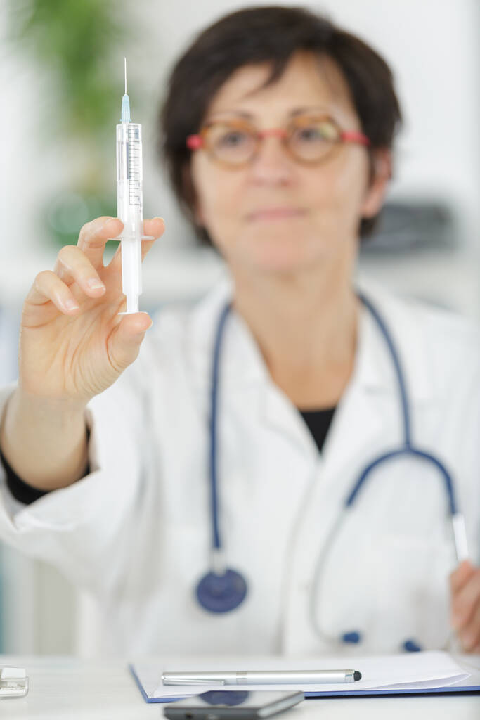Dojrzały lekarz pokazuje strzykawkę do pras ręcznych - Zdjęcie, obraz