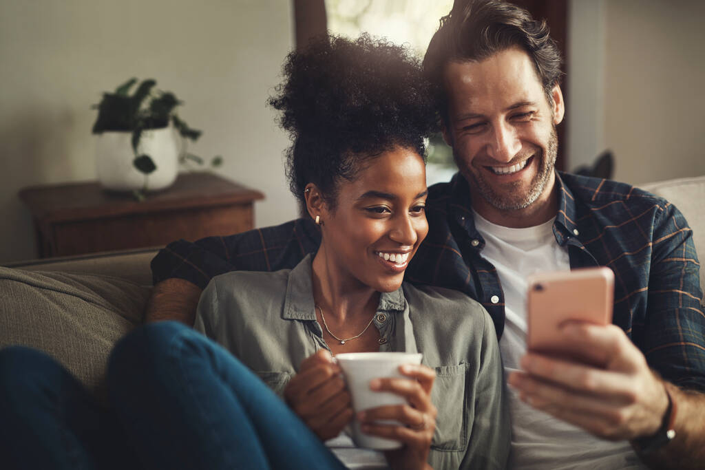 Guarda questi messaggi con me. una giovane coppia felice che usa un cellulare insieme mentre si rilassa su un divano a casa - Foto, immagini