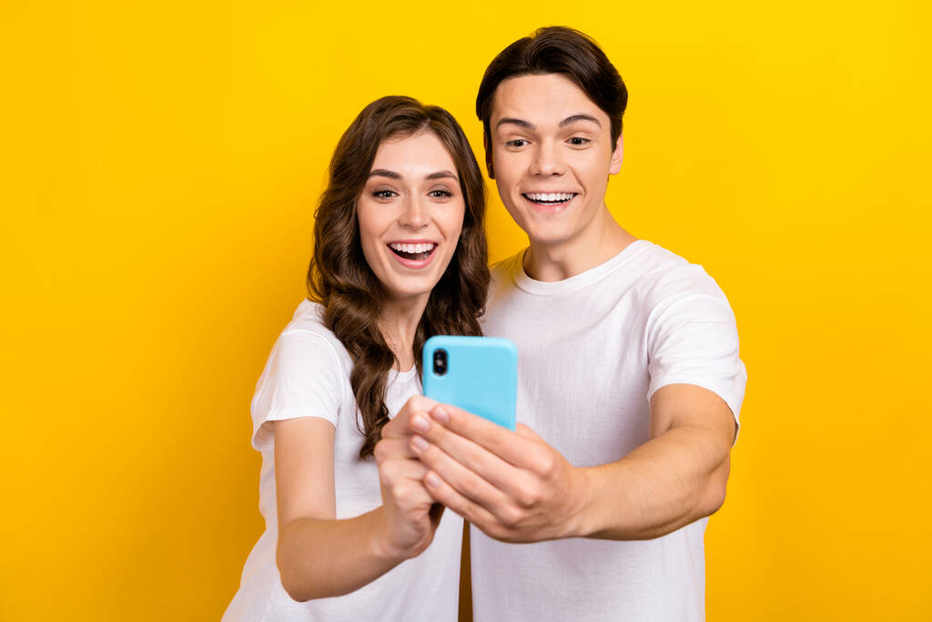Photo of pretty excited couple wear white t-shirts typing sms instagram twitter telegram facebook isolated yellow color background. - Photo, Image