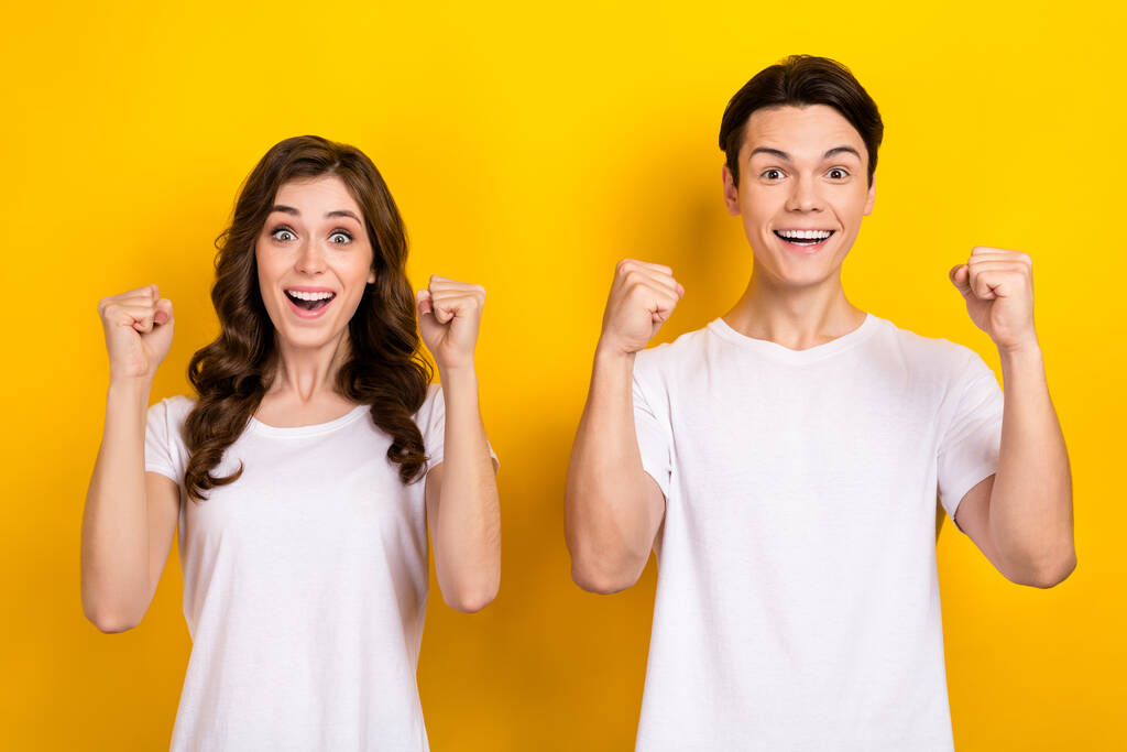 Φωτογραφία από δύο νέους ανθρώπους σηκώστε γροθιές επάνω φορούν λευκό t-shirt νέα ρούχα ψώνια ενθουσιασμένος γιορτάσουν τη νίκη απομονώνονται σε κίτρινο χρώμα φόντο. - Φωτογραφία, εικόνα