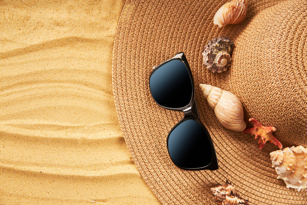 Koncept letních prázdnin. Slaměný klobouk, sluneční brýle a mušle na písečné pláži s kopírovacím prostorem pro text. Byt ležel, horní pohled - Fotografie, Obrázek