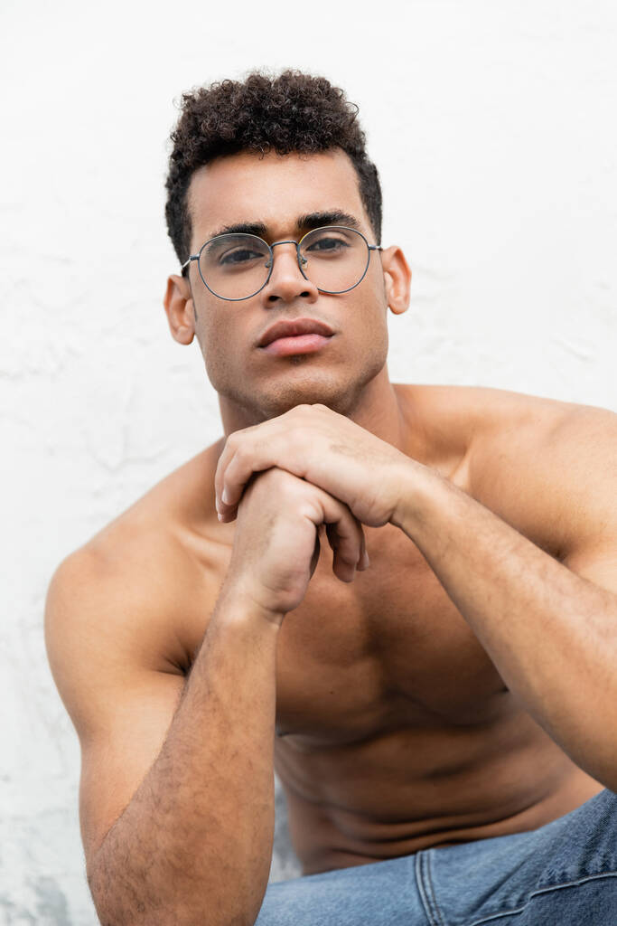 portrait of confident muscular young cuban man in stylish round-shaped eyeglasses looking at camera  - Photo, Image
