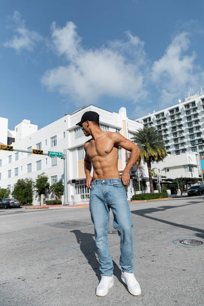sexy joven cubano en jeans y gorra de béisbol caminando en la calle urbana en Miam, verano  - Foto, imagen