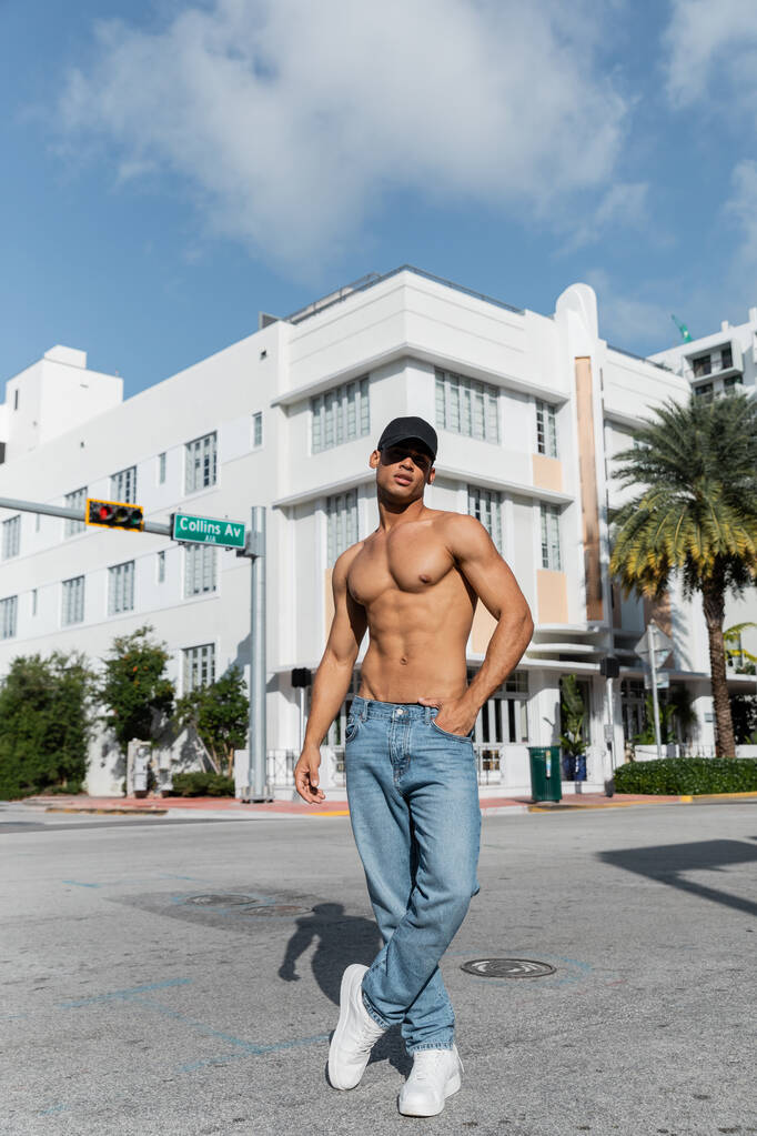 sin camisa hombre cubano sexy en jeans y gorra de béisbol caminando por la calle urbana en Miam, verano  - Foto, imagen