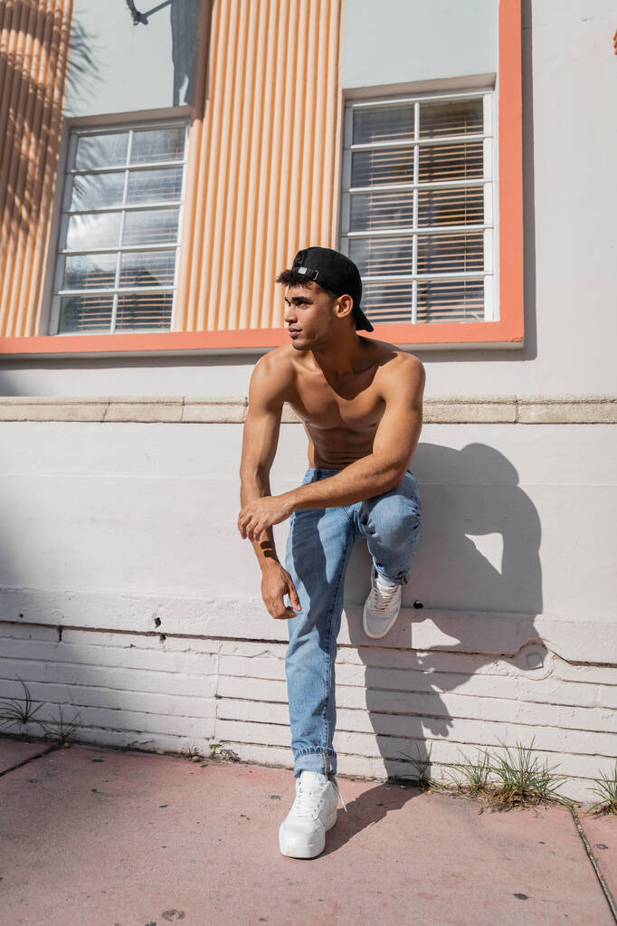 Kubańczyk z umięśnionym ciałem w czapce baseballowej i dżinsach stojących na ulicy w Miami - Zdjęcie, obraz