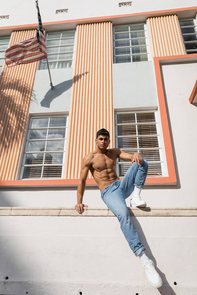 cuban man with muscular body posing in baseball cap and jeans on street in Miami - Photo, Image