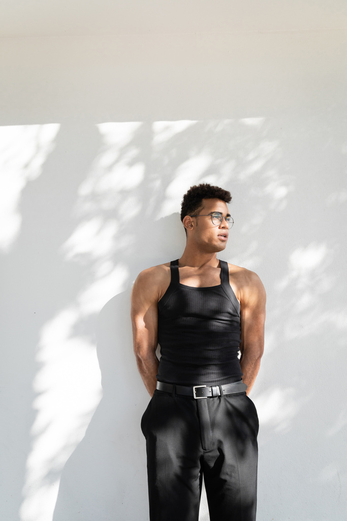 Junger, muskulöser junger kubanischer Mann mit Brille und modischem schwarzen Outfit schaut weg - Foto, Bild