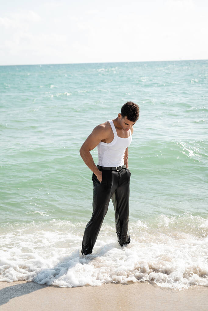 cuban man in wet clothes holding hands in pockets while standing in ocean water in Miami South Beach - Photo, Image
