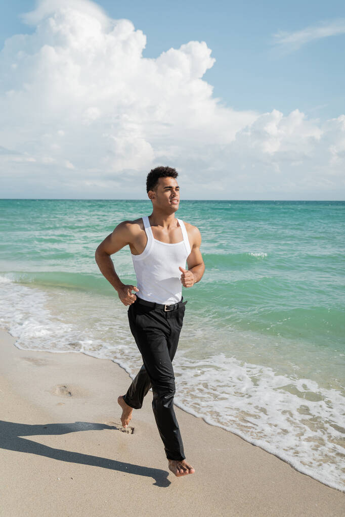 glücklicher kubanischer junger Mann läuft auf Sand in der Nähe des Ozeanwassers von Miami South Beach, Florida - Foto, Bild