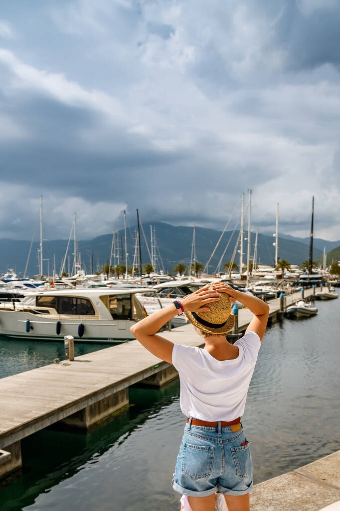 Vista traseira de uma mulher turística com um chapéu de palha em pé à beira-mar em Tivat, Kotor Bay, Montenegro - Foto, Imagem