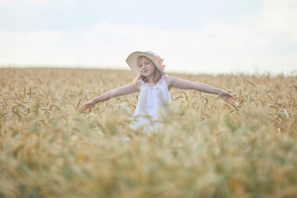 Портрет счастливой девушки в шляпе, стоящей на пшеничном поле  - Фото, изображение