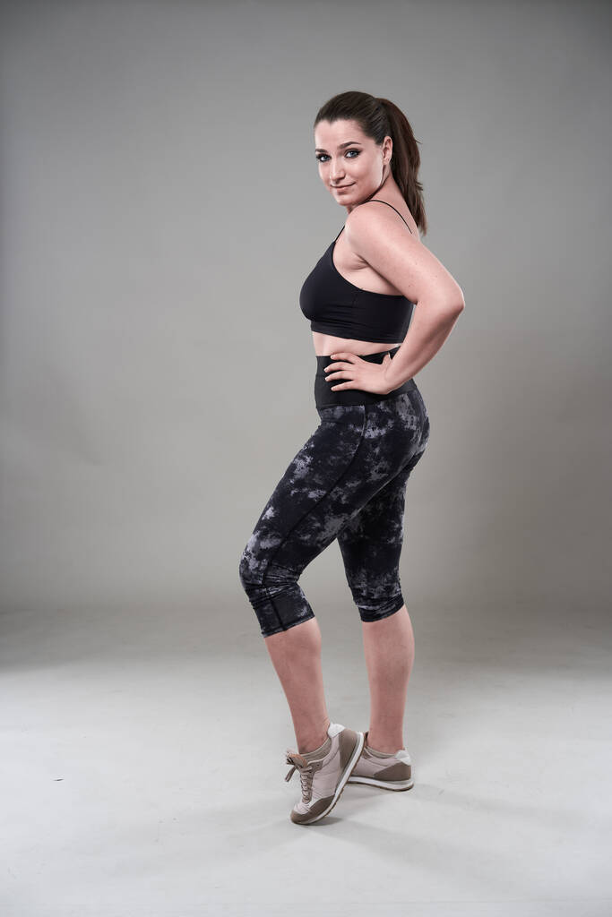Attractive plus size woman in fitness top and tights, gray background - Photo, Image