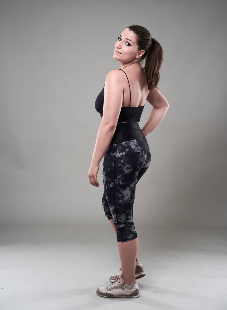 Ελκυστική συν μέγεθος γυναίκα σε fitness top και καλσόν, γκρι φόντο - Φωτογραφία, εικόνα