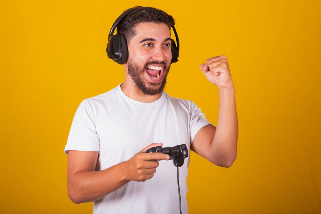 Szczęśliwy Brazylijczyk Ameryki Łacińskiej z słuchawkami i kontrolerem gier wideo, Świętowanie, kto wygrał, zwycięzca - Zdjęcie, obraz