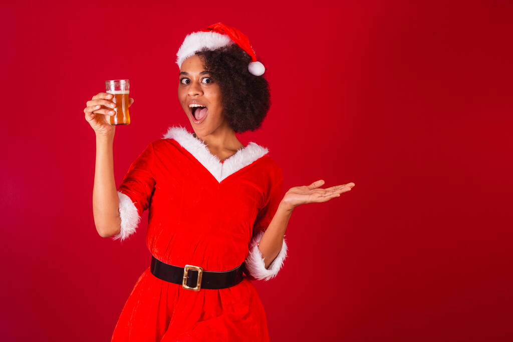 Güzel siyah Brezilyalı kadın, Noel Baba gibi giyinmiş, Mama Claus, elinde bir bardak bira tutuyor. - Fotoğraf, Görsel