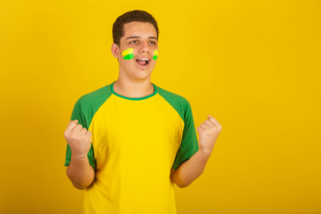 Genç Brezilyalı futbol fanatiği. Yeşil giyinmiş, sarı, çığlık atan bir gol. - Fotoğraf, Görsel