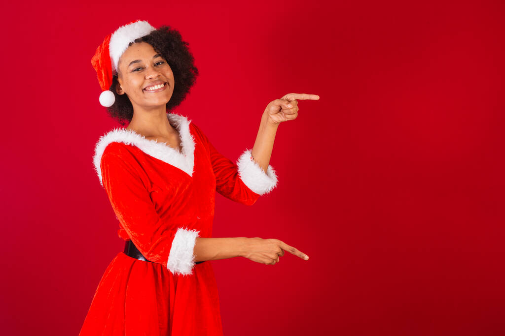 красива чорна бразильська жінка, одягнена як Санта-Клаус, мама-Клаус, представляє продукт або інформацію збоку
 - Фото, зображення