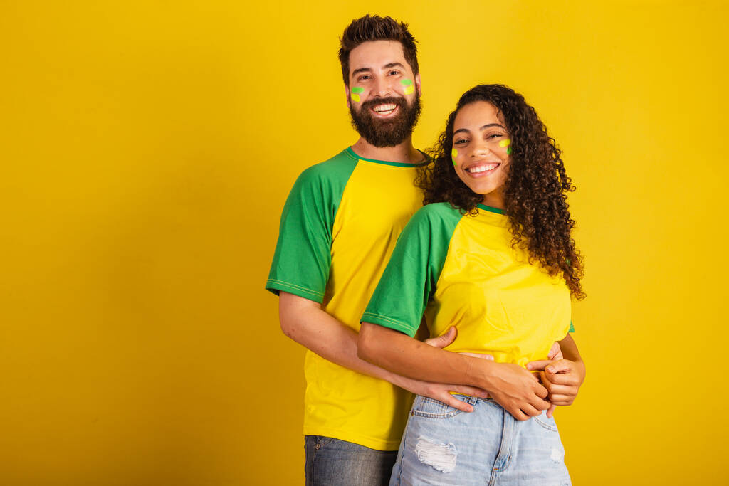 Braziliaanse voetbalsupporters, gekleed in de kleuren van het land, zwarte vrouw, blanke man. omarmd. - Foto, afbeelding