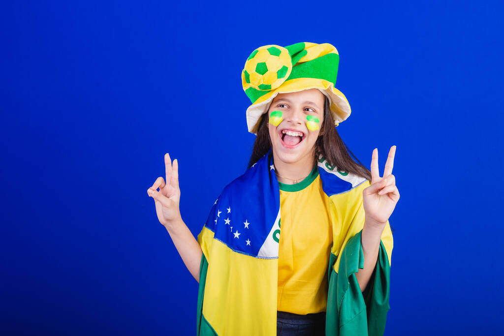 Młoda dziewczyna, fanka piłki nożnej z Brazylii. ubrany w kapelusz i flagę. dobre wibracje. - Zdjęcie, obraz