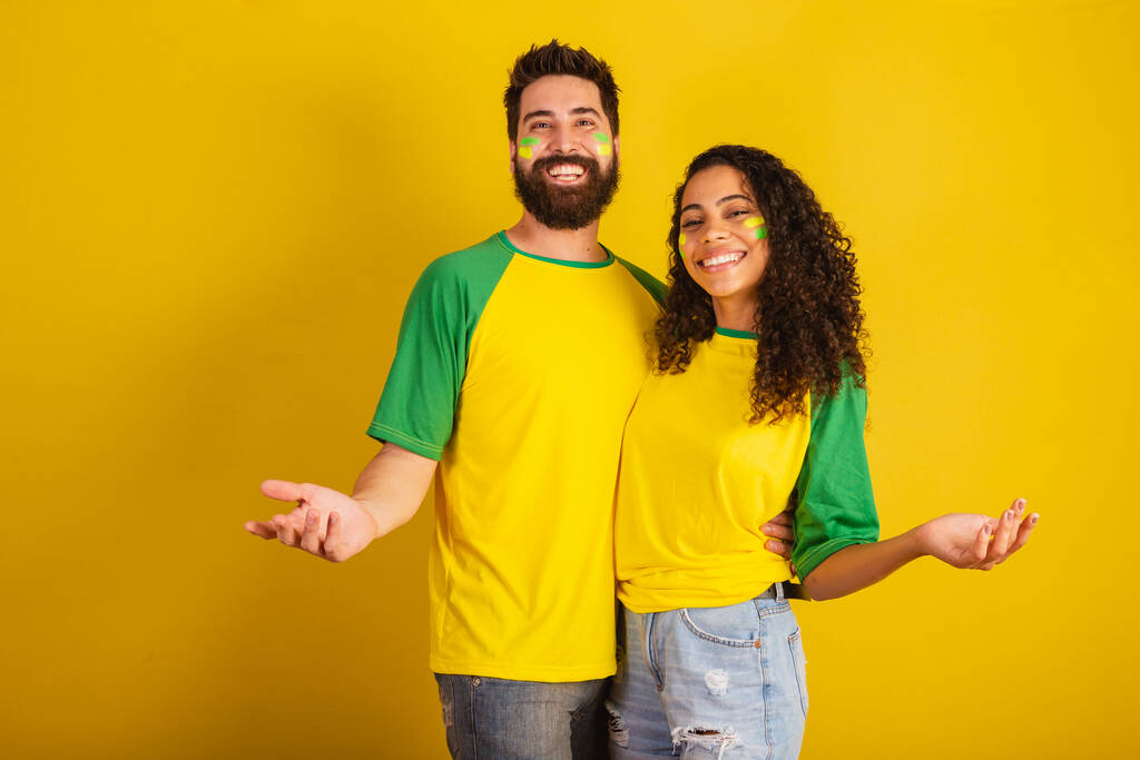 pareja de aficionados al fútbol brasileño, vestidos con los colores de la nación, mujer negra, hombre caucásico. Bienvenida. Brazos abiertos - Foto, Imagen