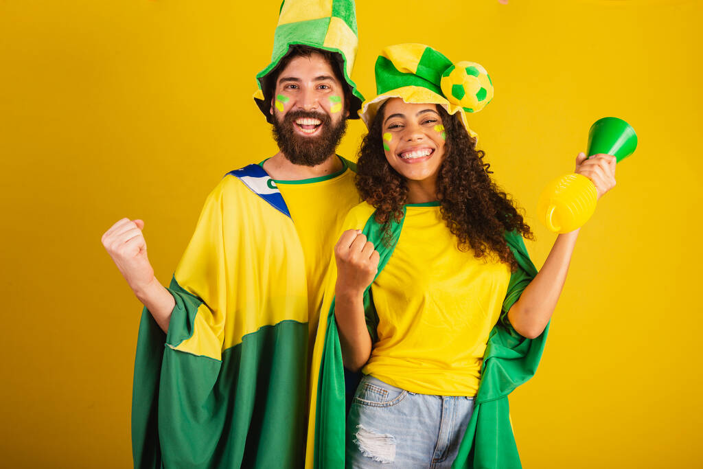 couple de supporters brésiliens de football, vêtus aux couleurs de la nation, femme noire, homme caucasien. utilisant le drapeau et les accessoires - Photo, image