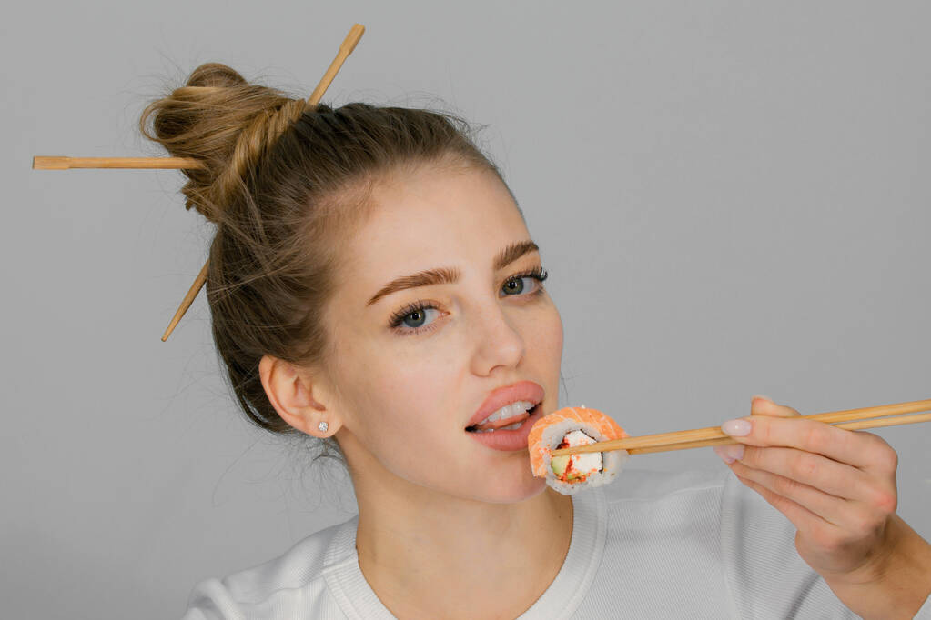 Comiendo sushi japonés. Mujer joven y bella comiendo sushi con palillos, aislada en blanco. Rollo de sushi con palillos. Comida japonesa saludable - Foto, imagen