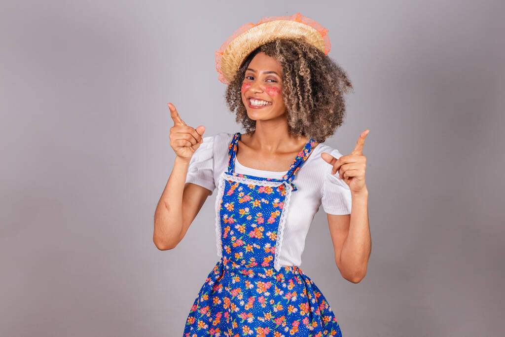 Молодая бразильская женщина в кантри-одежде, одетая для Фесты Джунины. Фестиваль Святого Иоанна. оптимистично и уверенно указывая на небо. - Фото, изображение