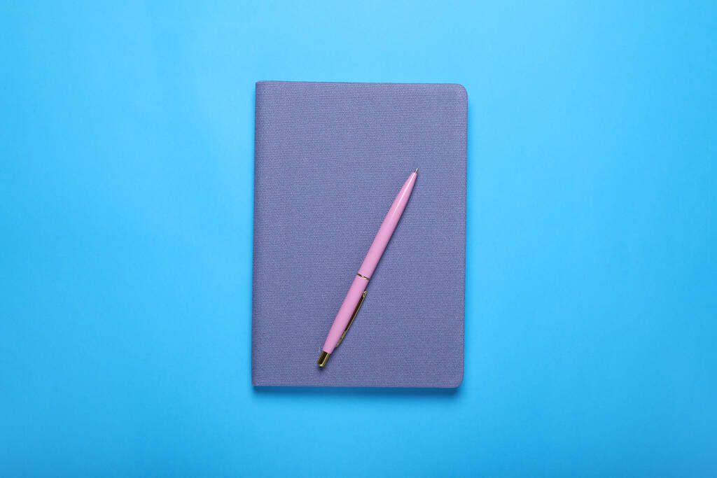 Gesloten notitieboek en pen op lichtblauwe achtergrond, bovenaanzicht - Foto, afbeelding