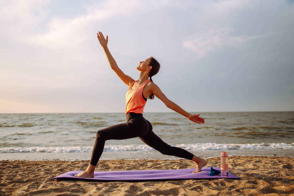 Actieve levensstijl. Jonge mooie vrouw doet 's morgens yoga op het strand bij zonsopgang, buiten aan het stretchen. Begrip sport, sporttraining, yoga of fitness. - Foto, afbeelding