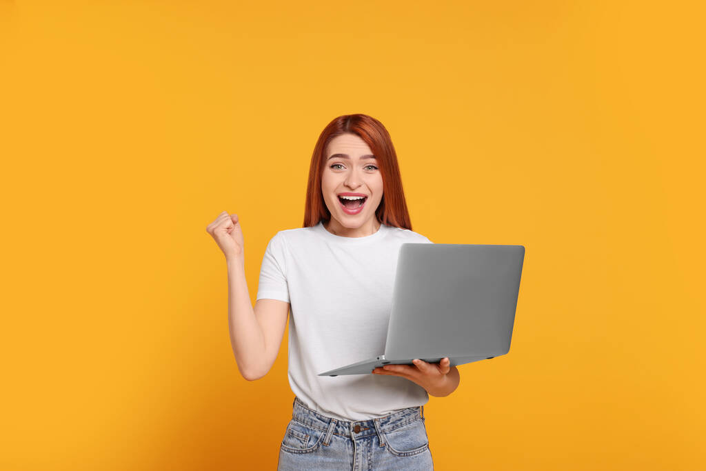 gelukkig jong vrouw met laptop op gele achtergrond - Foto, afbeelding