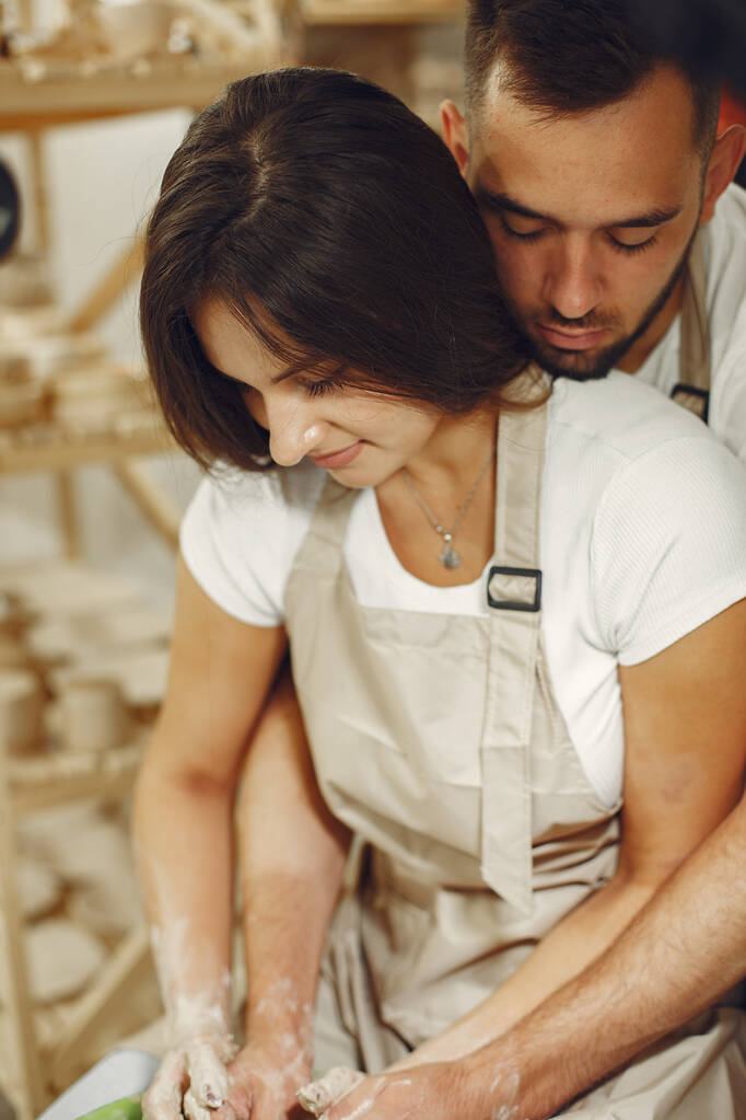 Mutual creative work. Young beautiful couple in casual clothes and aprons. People creating a bowl on a pottery wheel in a clay studio. - Foto, afbeelding