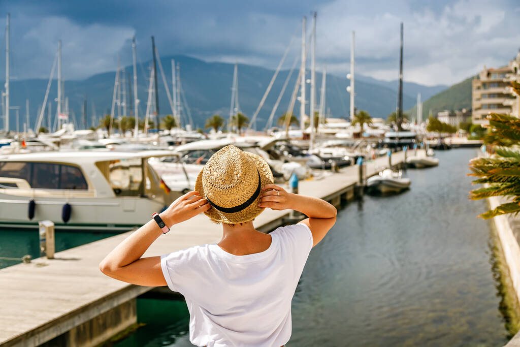 Οπίσθια όψη τουρίστριας με ψάθινο καπέλο που κοιτάζει τα γιοτ στο λιμάνι Τίβατ, Κόλπος Κότορ, Μαυροβούνιο - Φωτογραφία, εικόνα