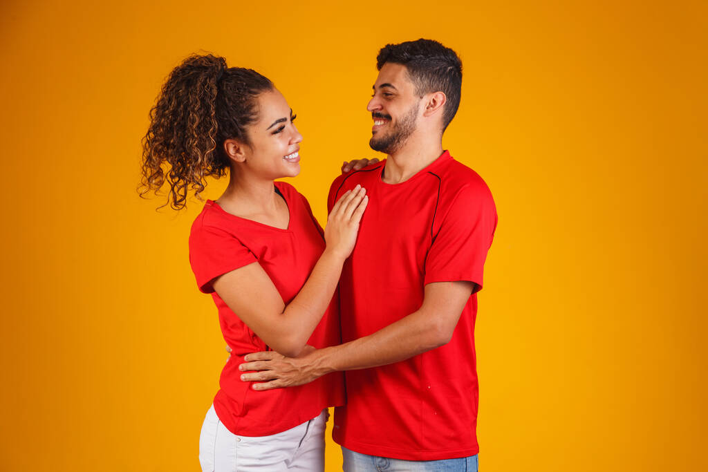 Porträt eines zufriedenen Paares in einfachen Kleidern, das in die Kamera lächelt, während die Frau ihren Kopf auf die männliche Schulter legt, isoliert über gelbem Hintergrund ist er überrascht und glücklich - Foto, Bild