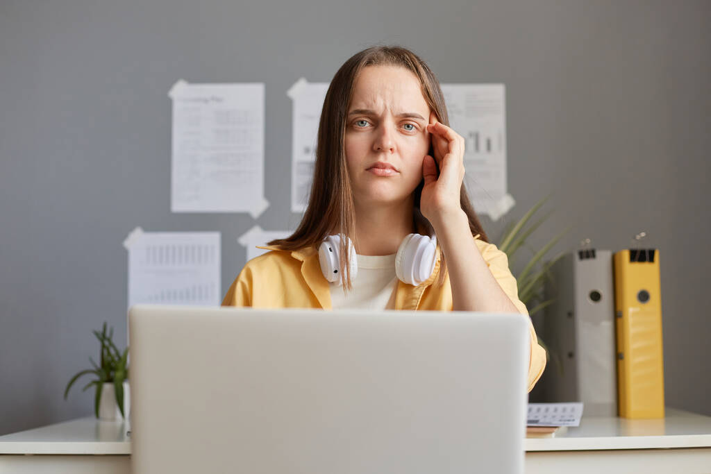 Väsynyt nainen istuu tietokoneen edessä tunne väsymystä kärsimystä päänsärky viettää pitkiä tunteja tehdä online-työtä pitämällä kannettavaa tietokonetta hierova temppeli katselee kameraa. - Valokuva, kuva