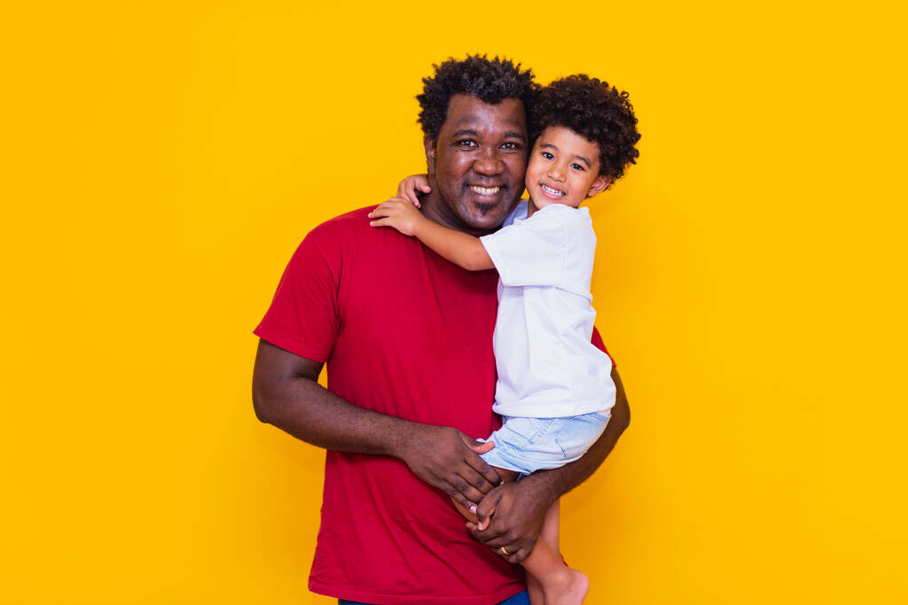Vader en afro zoon op gele achtergrond glimlachend. Vaderdag concept - Foto, afbeelding