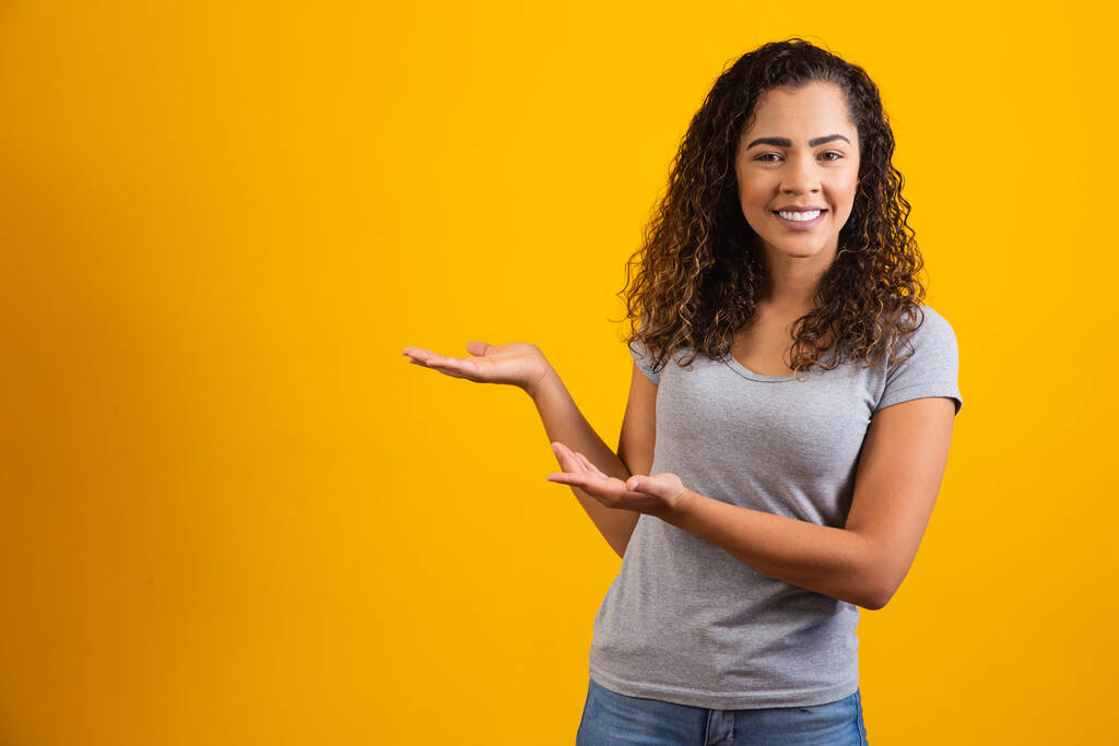 Afro woman pointing in yellow background with space for the text - Photo, Image